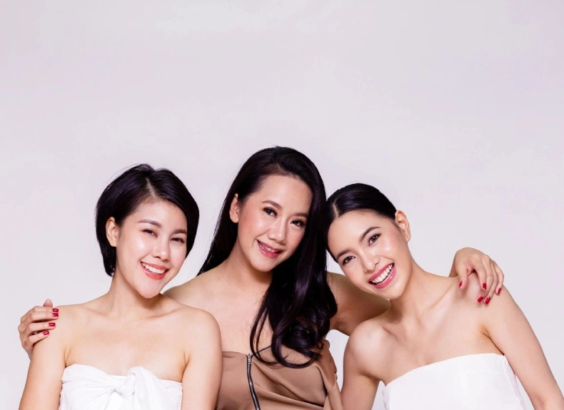 Three women posing for a picture in front of a white wall.